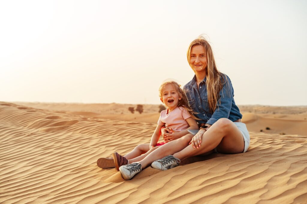 Mother and daughter sitting together on sand dune in the Dubai desert